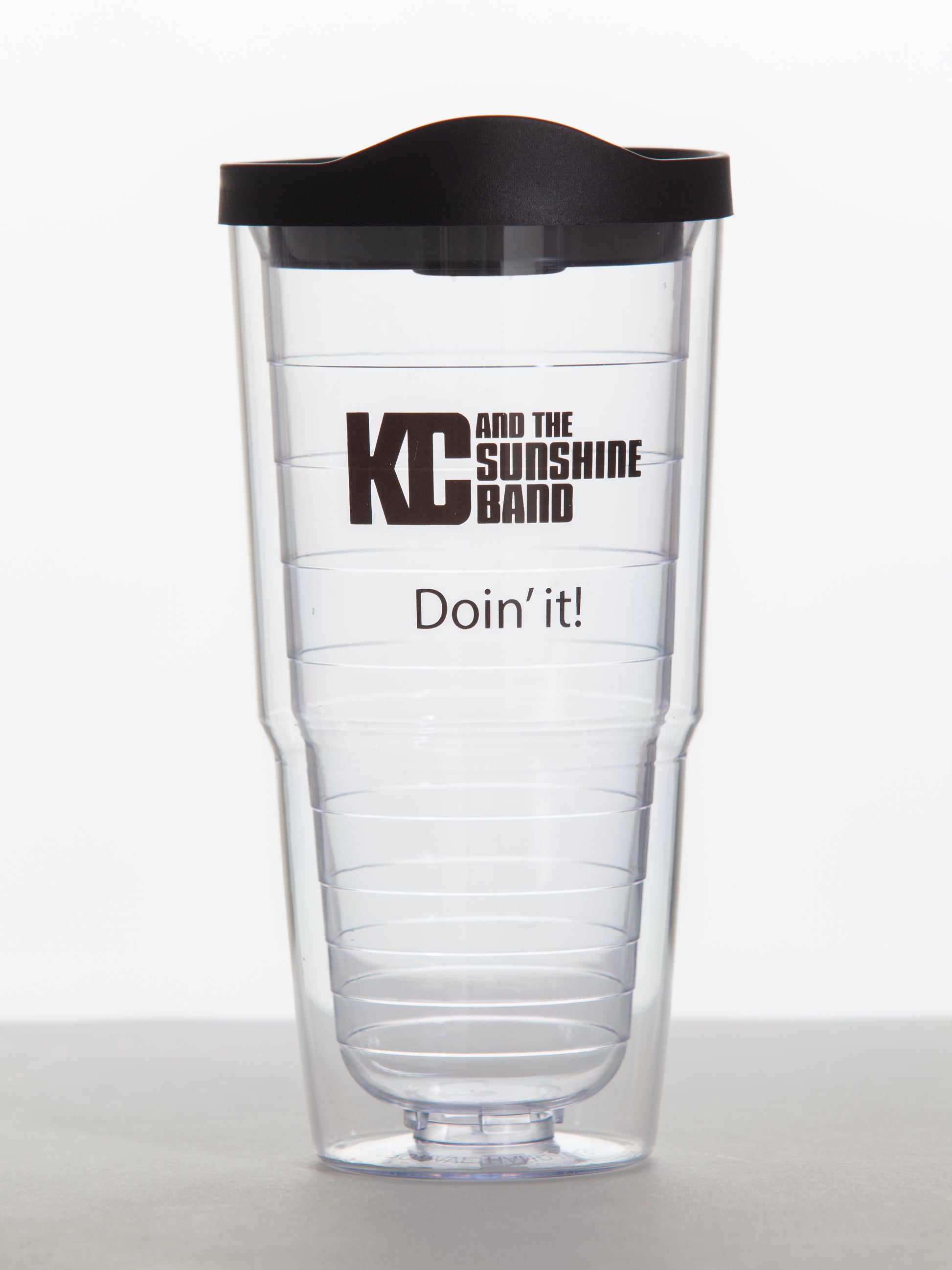 A clear plastic tumbler with a black lid, featuring the text 'KC and the Sunshine Band' and 'Doin' it!' printed in black.